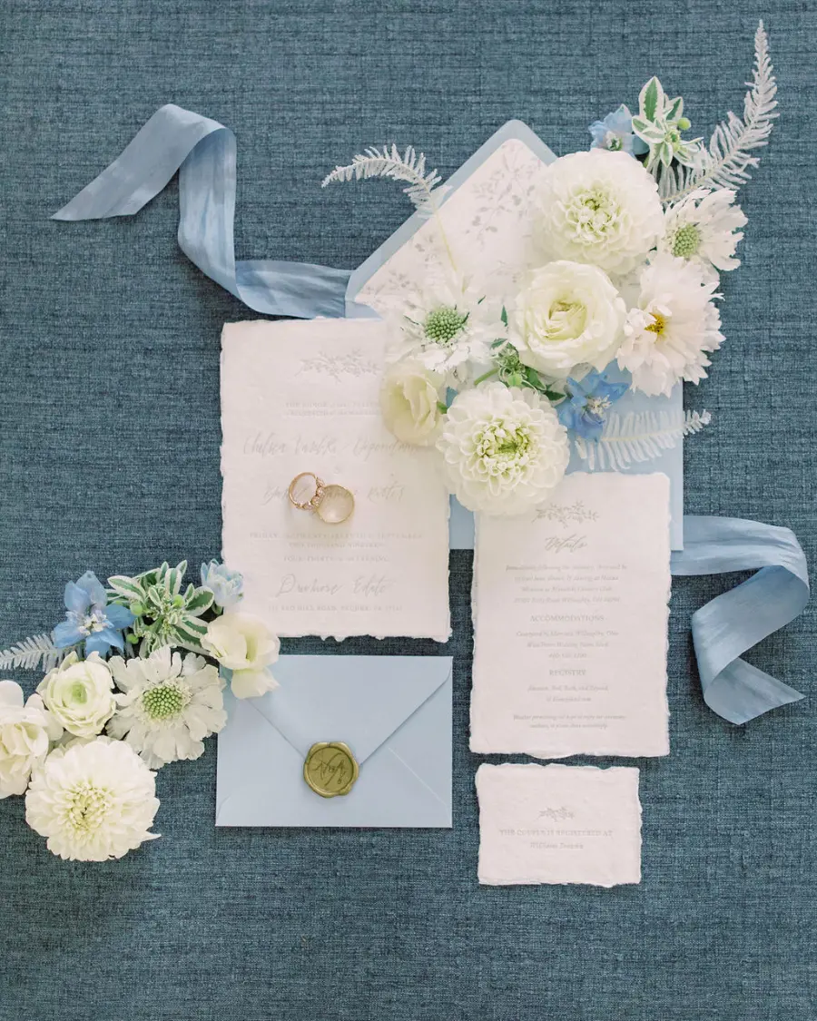 Convite branco com envelope azul e flores brancas e azuis ao redor.