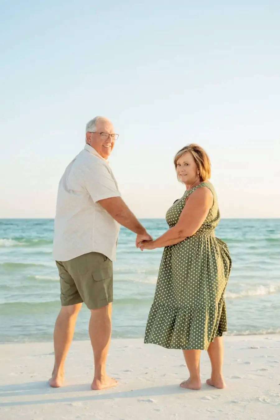 Casal maduro de mãos dadas caminhando na praia durante o pôr do sol