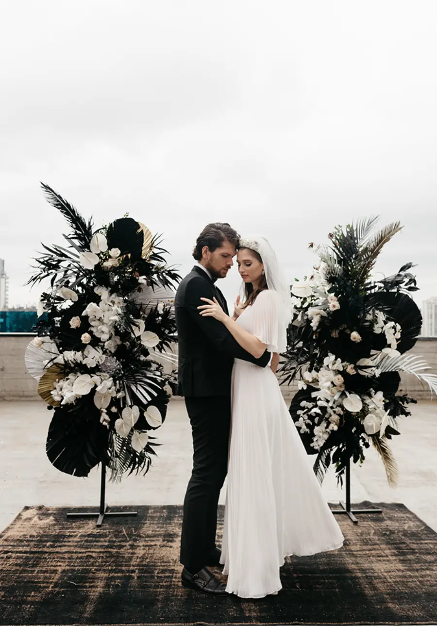 Casal em altar moderno com arranjos preto e branco em contraste elegante.