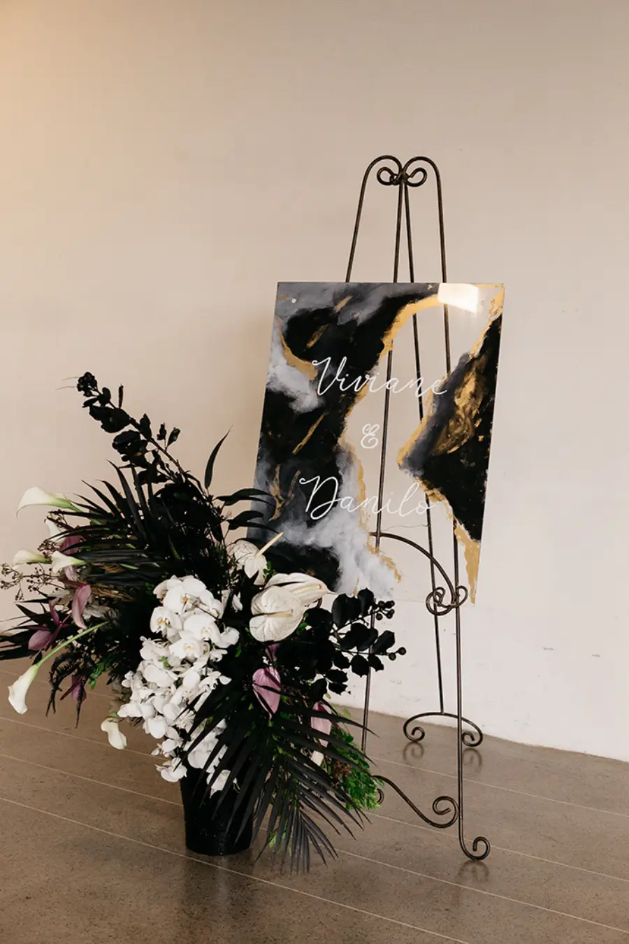 Placa de boas-vindas em preto e dourado com arranjo floral branco e preto.