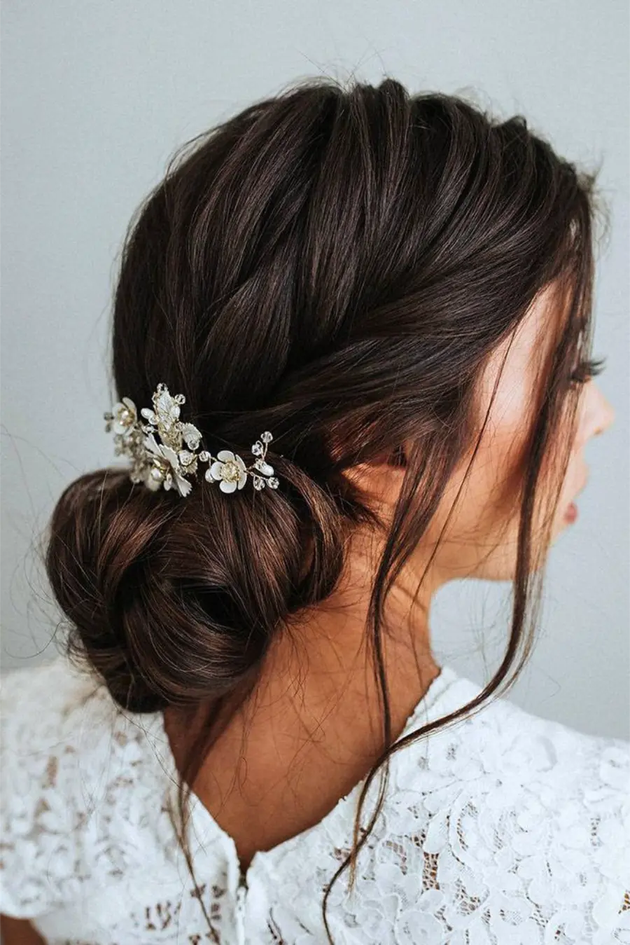 Penteado de noiva com coque baixo e acessório prateado com flores delicadas.