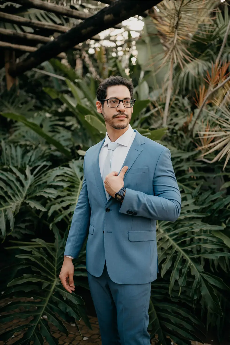 Noivo com terno azul serenity e gravata clara posando em ambiente natural.