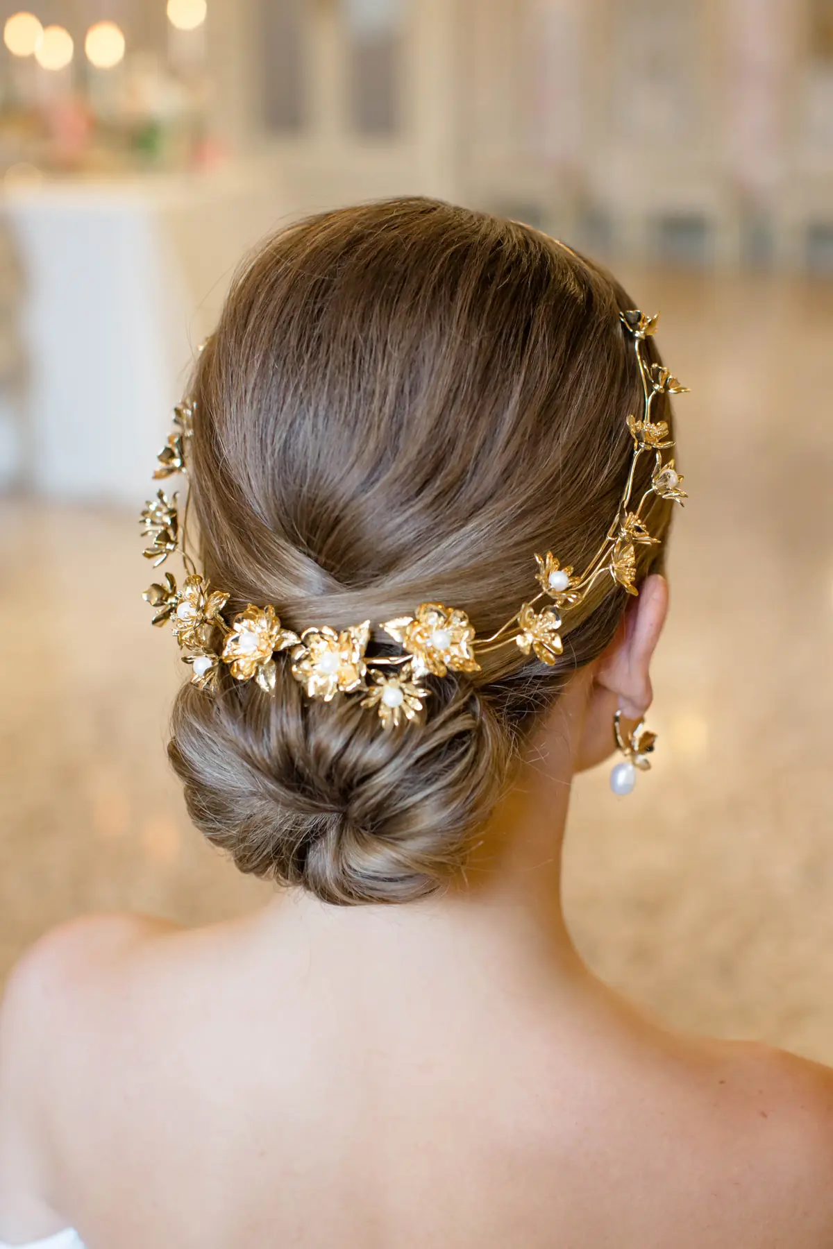 Noiva com coque baixo elegante adornado por acessório dourado em formato de flores com pérolas