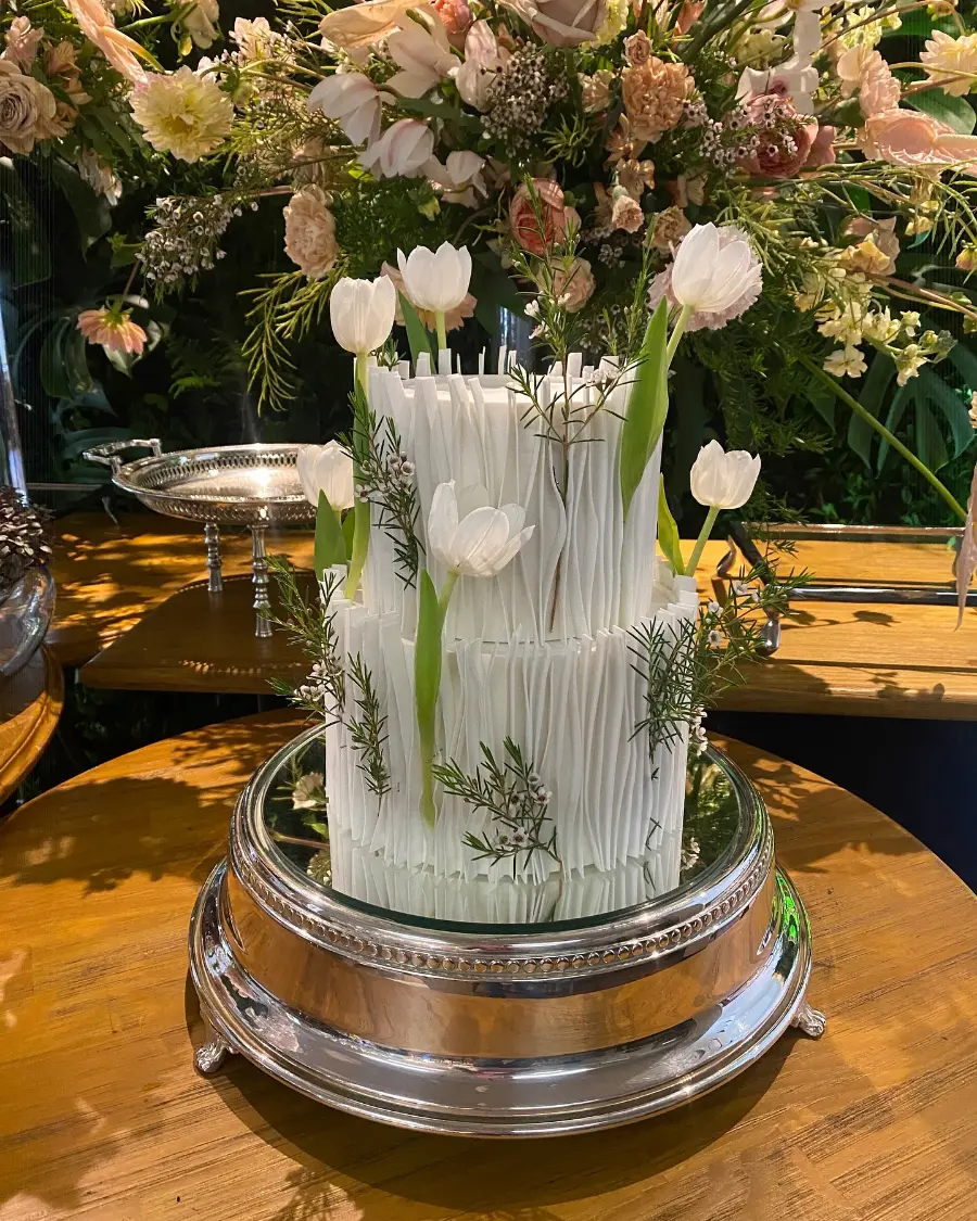 Bolo de casamento branco de dois andares com textura vertical e decoração de tulipas brancas naturais.