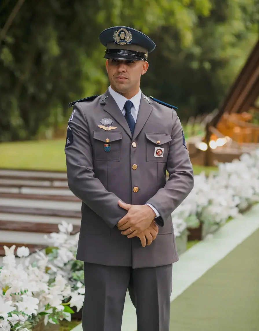 Noivo em uniforme militar cinza de gala aguarda no altar em cerim&ocirc;nia de casamento ao ar livre com flores brancas.