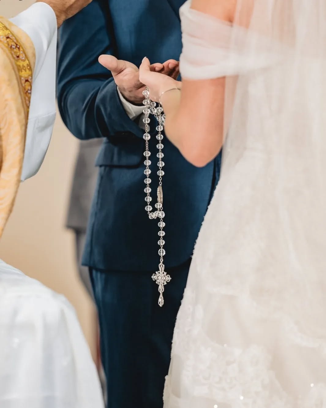 Casal durante a cerimônia com a noiva segurando um terço transparente.