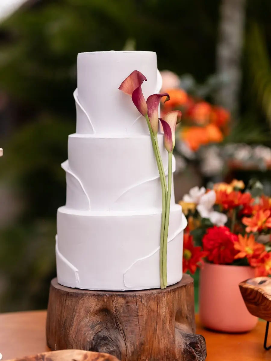 Bolo fake branco de quatro andares minimalista com flores roxas na lateral em base de madeira rústica