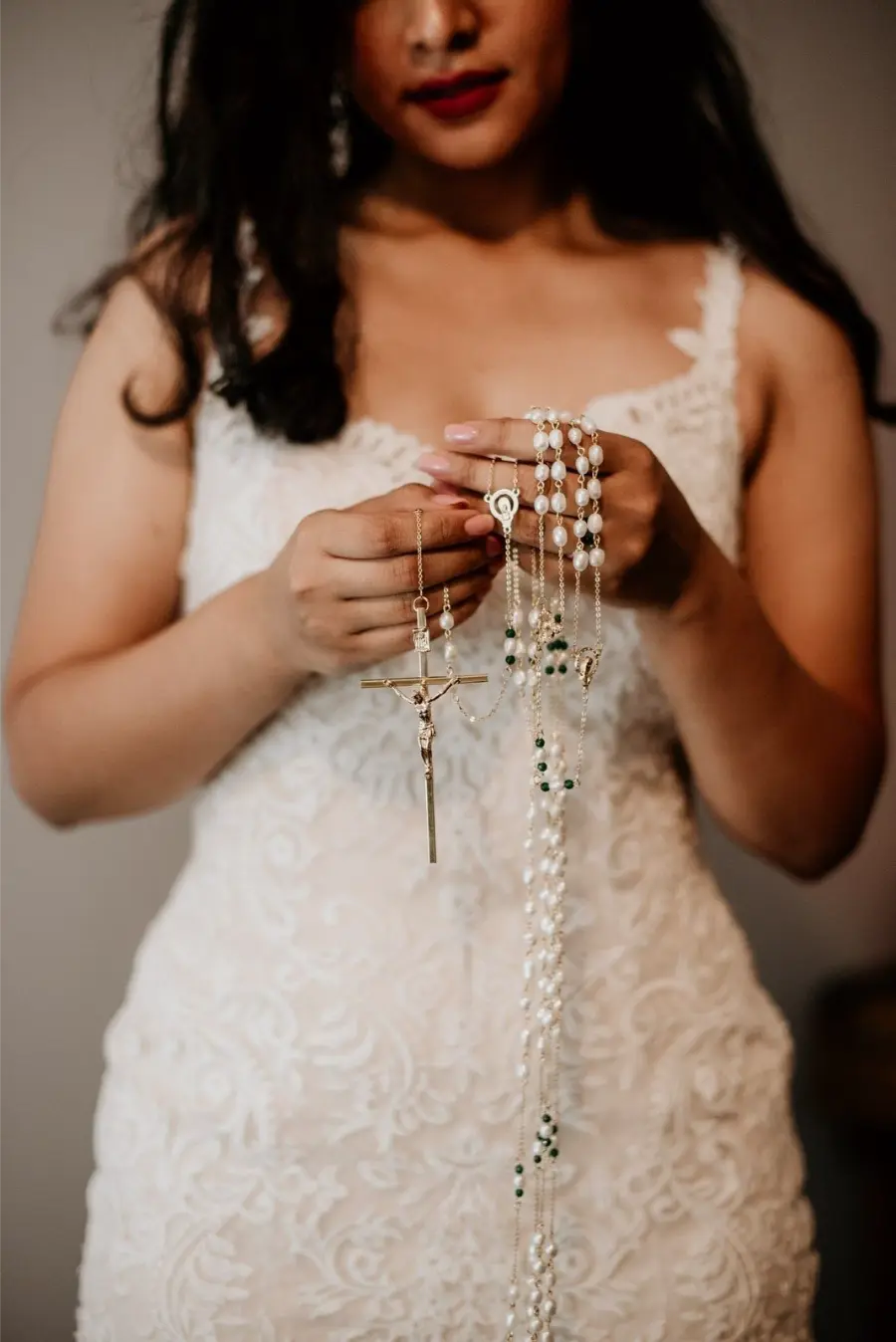 Noiva de vestido rendado segurando terço dourado com contas brancas e verdes.
