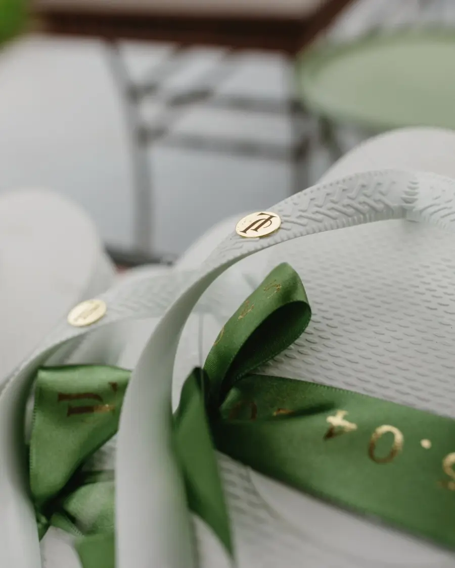 Chinelo branco de lembrancinha de casamento com fita verde personalizada em dourado e iniciais gravadas nos detalhes metálicos.