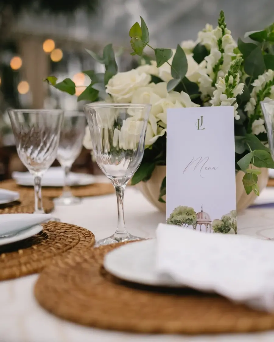 Mesa de casamento decorada com flores brancas e cardápio personalizado com monograma JL e ilustração botânica.