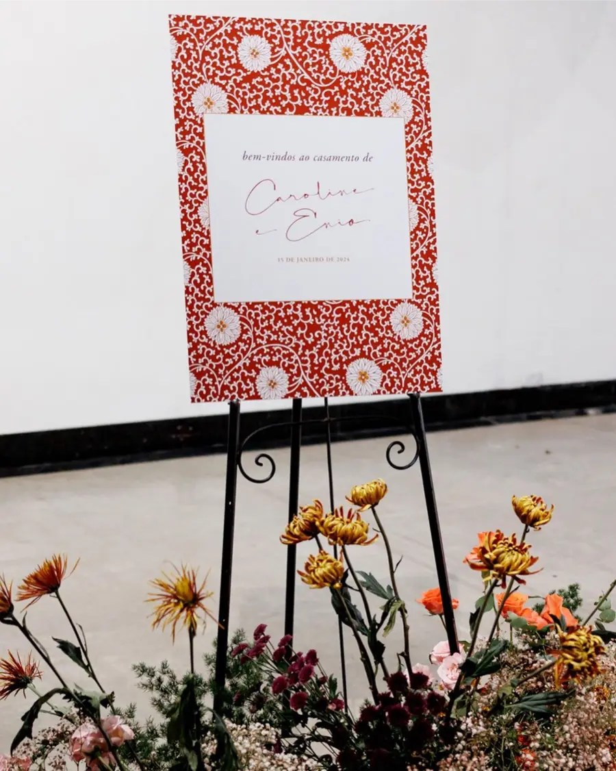 Placa de boas-vindas para casamento de Caroline e Ênio com padrão floral laranja em cavalete com flores
