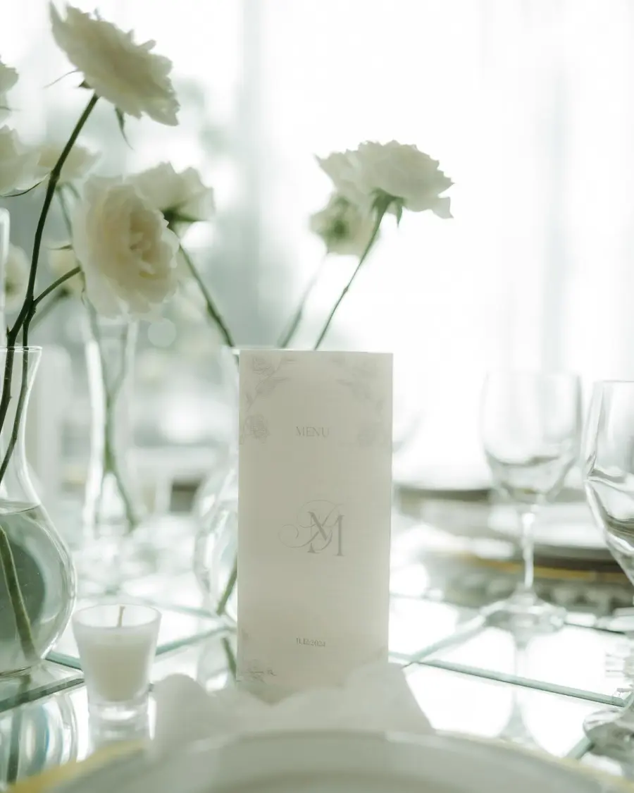 Mesa de casamento minimalista com vela branca, flores brancas em vaso de vidro e taças de cristal