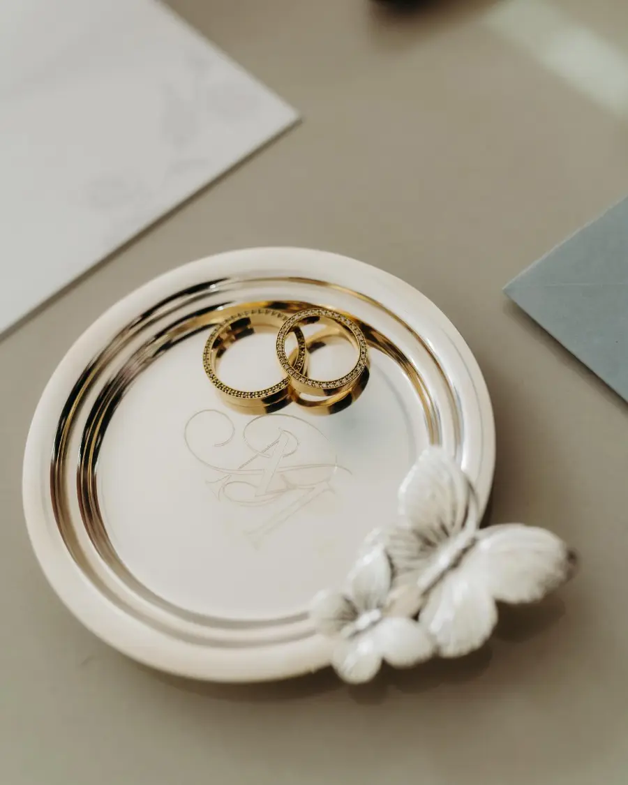 Alianças de ouro sobre prato espelhado decorado com flores secas brancas e papelaria de casamento