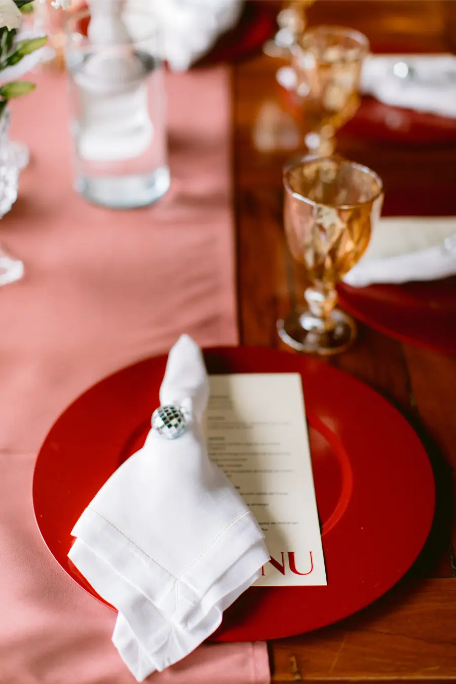 Mesa posta de casamento com prato vermelho, guardanapo branco com porta-guardanapo decorativo e cardápio personalizado.