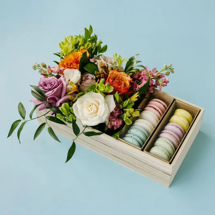 Caixa de presente combinando flores coloridas e macarons de diferentes sabores em divisórias organizadas.