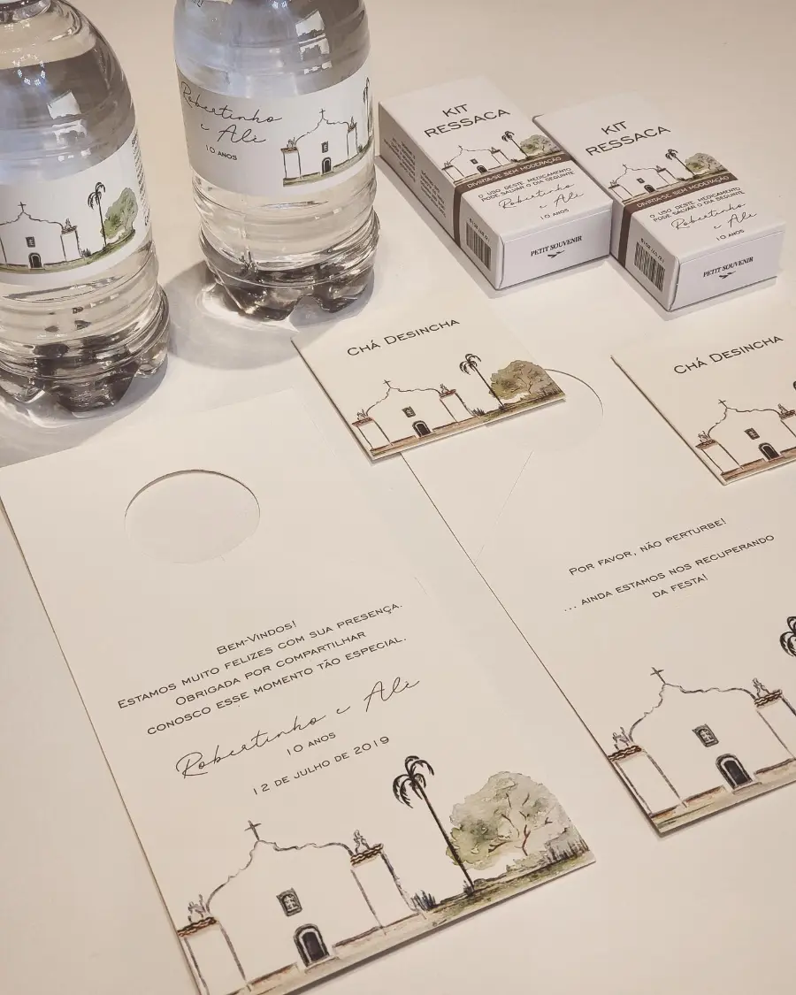 Kit de lembrancinhas de casamento com garrafinhas de água, kit ressaca e chá, todos personalizados com ilustração de igreja colonial.