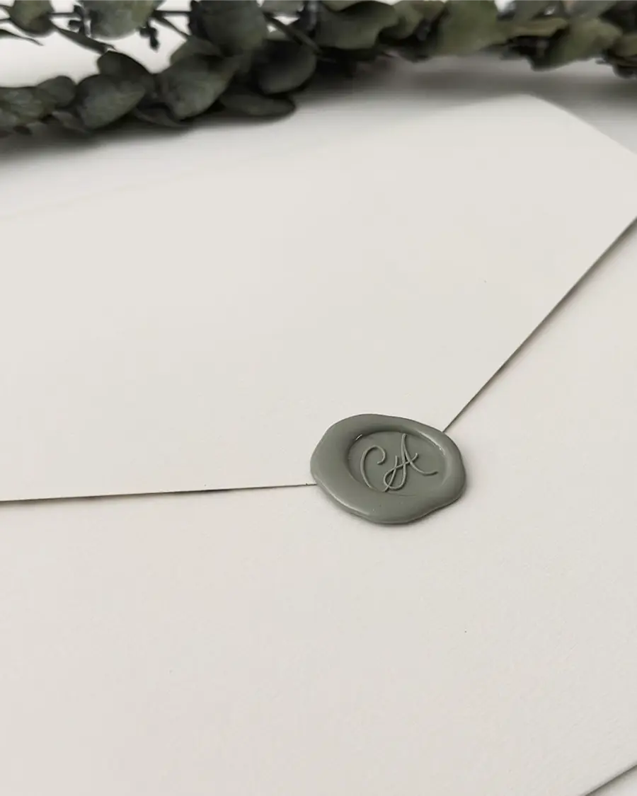 Envelope de convite de casamento em tom neutro com lacre de cera verde personalizado com iniciais dos noivos.