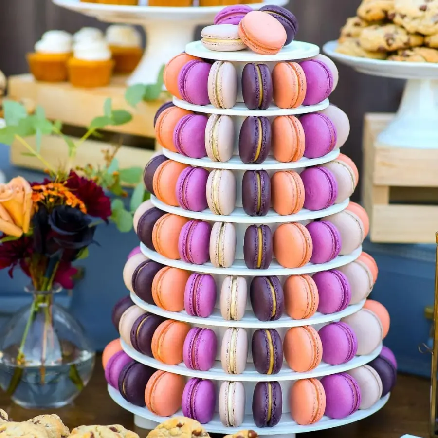 Torre de macarons em camadas de cores vibrantes como roxo, lilás, laranja e rosa, compondo a mesa de doces da festa.
