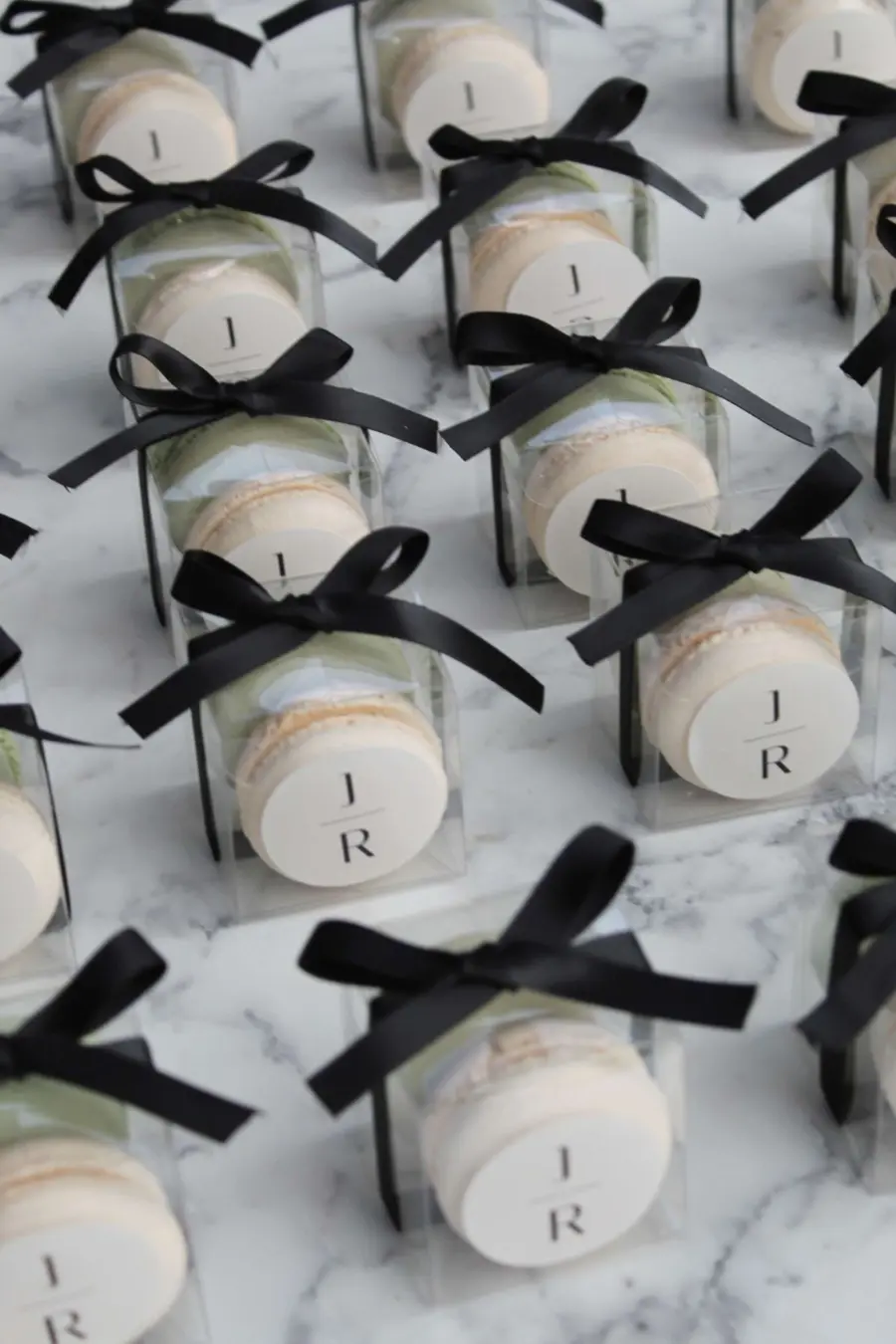 Macarons embalados em caixinhas transparentes com laço preto e iniciais personalizadas.