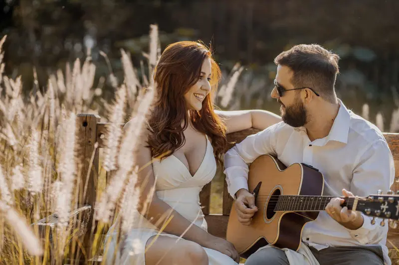 casal tocando viol&atilde;o em meio aos capim dos pampas