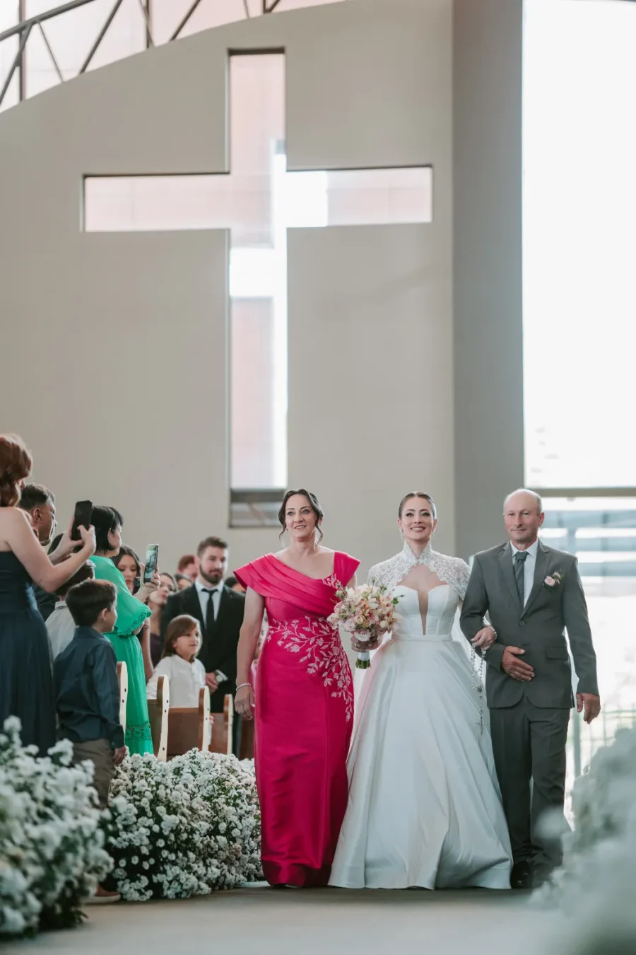entrada da noiva na igreja com am&atilde;e de vestido rosa e pai de terno cinza