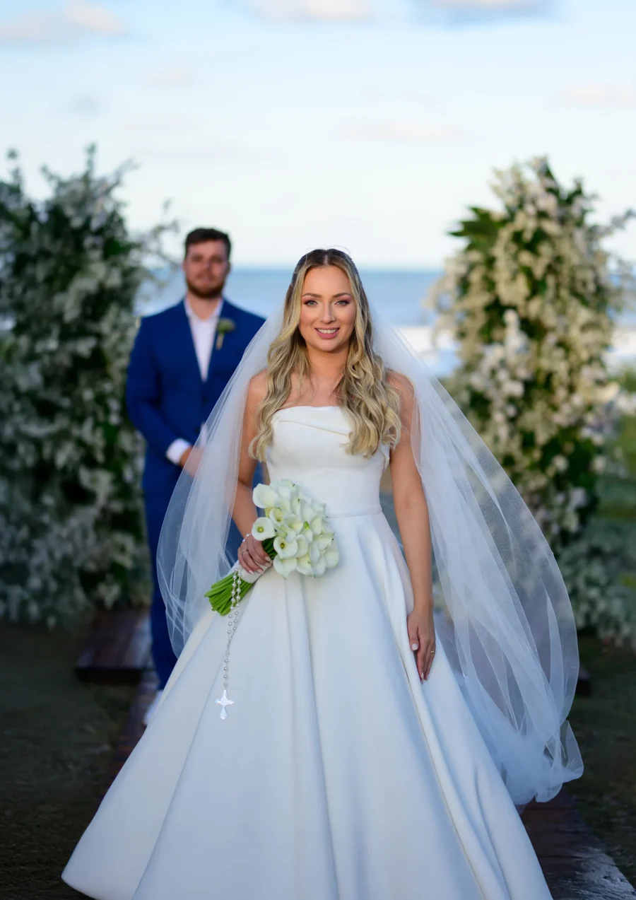 noiva com buque e noivo com terno azul ao fundo