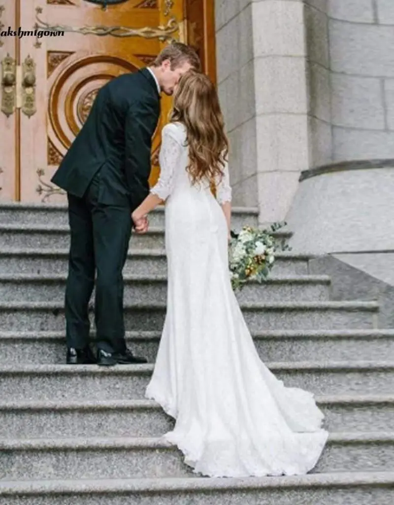 noivos se beijando na escada. Ela est&aacute; usando vestido de noiva branco rendado de comprimento longo com mangas tr&ecirc;s quartos.