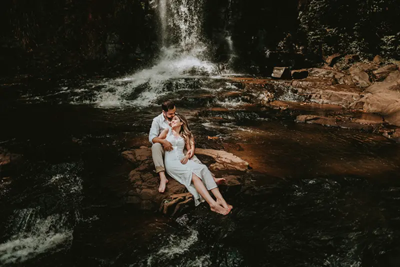 ensaio de noivado na cachoeira com casal sentado na pedra 