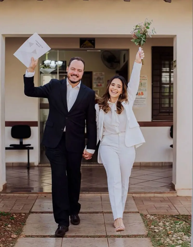 noivos saindo do cart&oacute;rio felizes segurando a certid&atilde;o de casamento