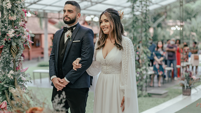 noiv acom vestido com capa rendada ao lado do noivo de terno preto e cinza