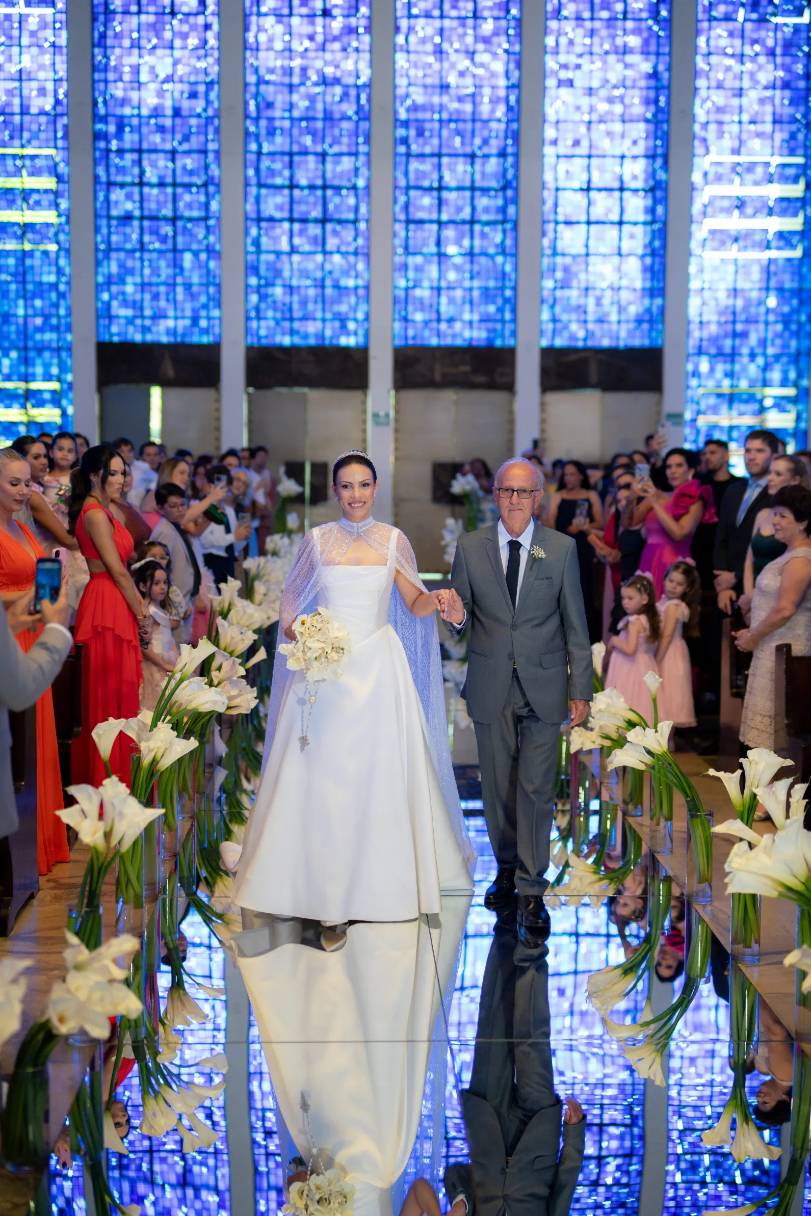 mulher com vestido de noiva com capa entrando na igreja ao lado do pai