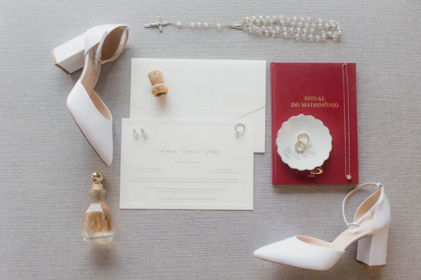 sapato de noiva ao lado de perfume e convite de casamento