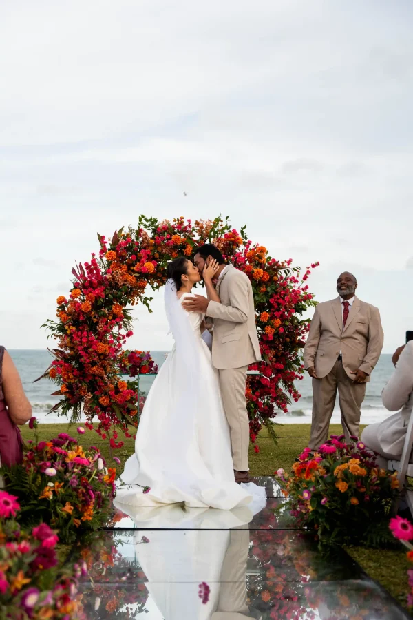 noivos se beijando em frente a altar na praia rosa e laranja