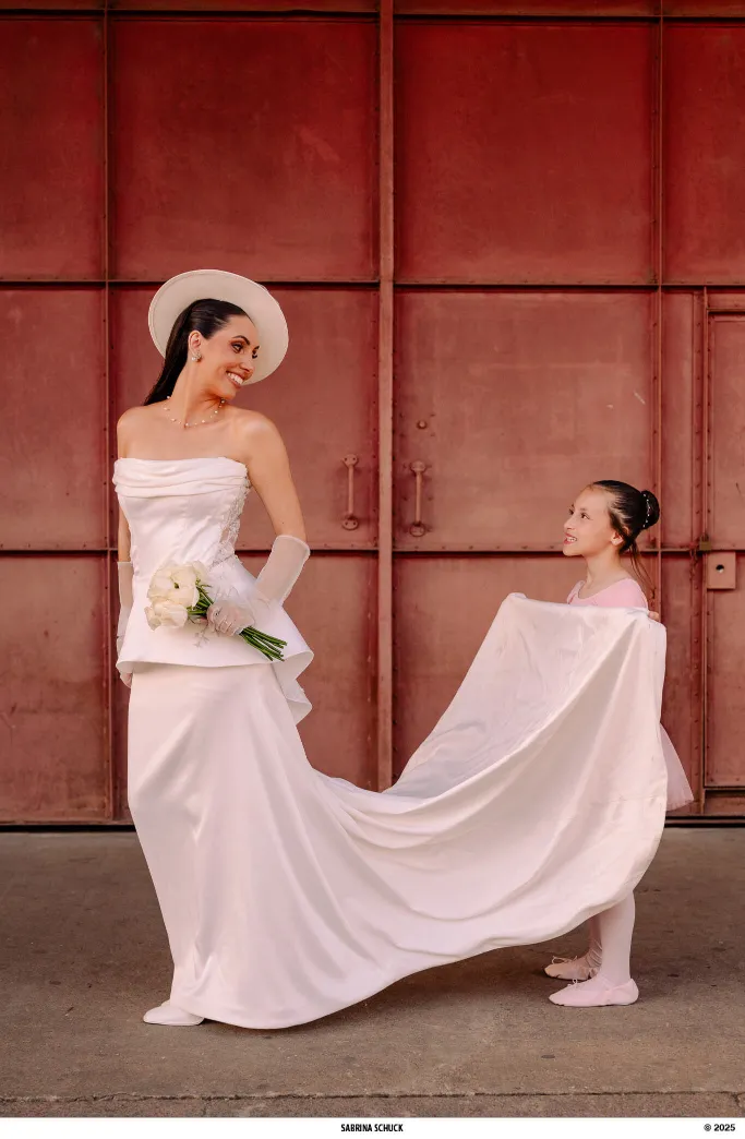 mulher com vestido de noiva com corset e chapéu e menina segurando o a saia do vestido